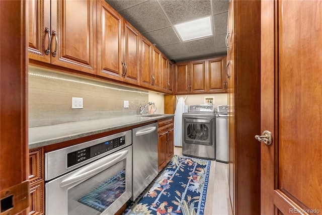 kitchen with stainless steel appliances, sink, light wood-type flooring, washing machine and clothes dryer, and a drop ceiling