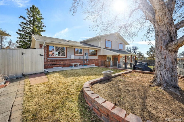 rear view of property with brick siding, fence, stucco siding, a yard, and a gate