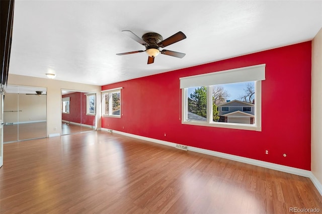 unfurnished room with a healthy amount of sunlight, a ceiling fan, baseboards, and wood finished floors