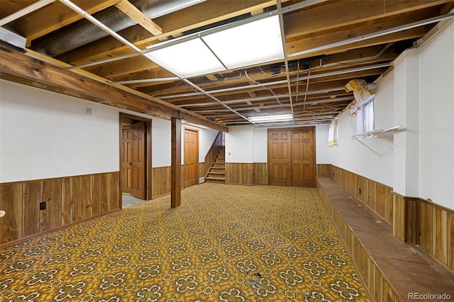 below grade area with a wainscoted wall, wooden walls, and stairway