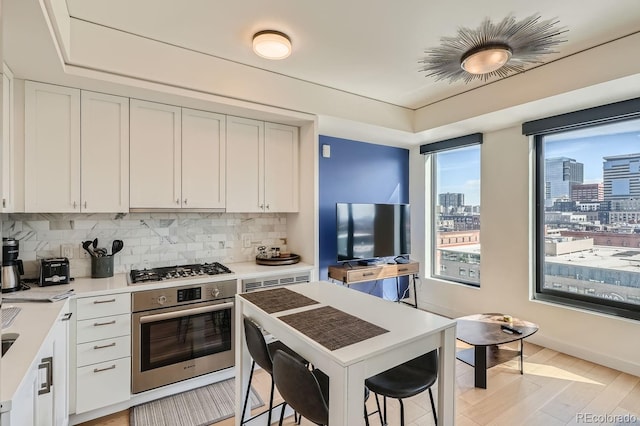 kitchen featuring appliances with stainless steel finishes, white cabinets, light wood-type flooring, and backsplash