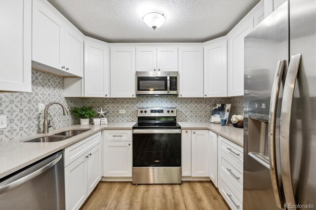 kitchen with appliances with stainless steel finishes, light wood-type flooring, white cabinets, backsplash, and sink