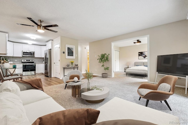 living room with light wood-type flooring, ceiling fan, and a textured ceiling