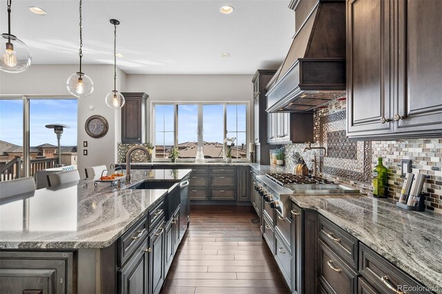 10468 Ladera Dr, Lone Tree, CO 80124 - kitchen with premium range hood, stainless steel gas cooktop, backsplash, light stone countertops, and dark wood-style flooring