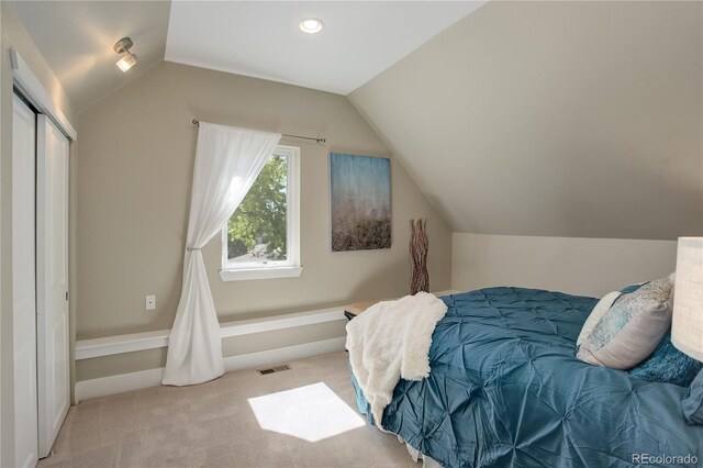 bedroom with light carpet, lofted ceiling, and a closet