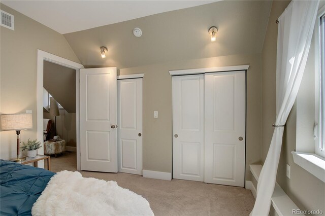 bedroom featuring lofted ceiling, light colored carpet, and multiple closets