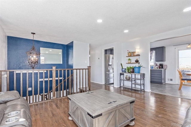 living area with a textured ceiling, wood finished floors, visible vents, and a notable chandelier