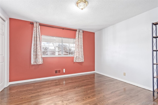 spare room featuring baseboards, a textured ceiling, visible vents, and wood finished floors