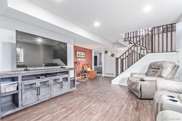 living room featuring baseboards, visible vents, wood finished floors, stairs, and a textured ceiling