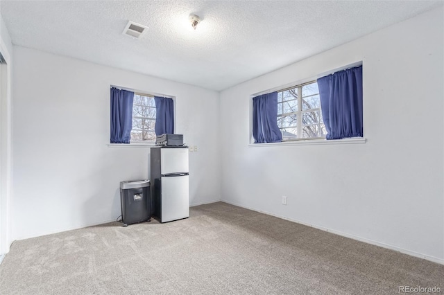 unfurnished bedroom featuring freestanding refrigerator, carpet flooring, visible vents, and a textured ceiling