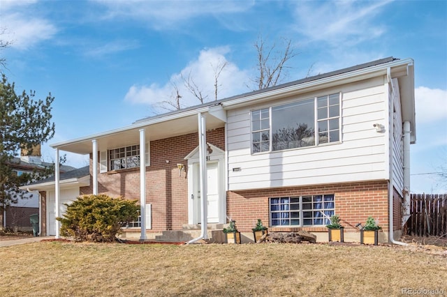 split foyer home featuring brick siding, a front yard, and fence