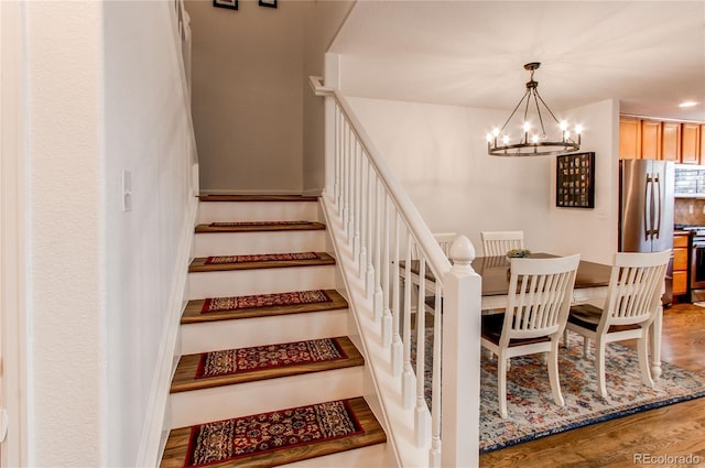 staircase with a notable chandelier and wood finished floors