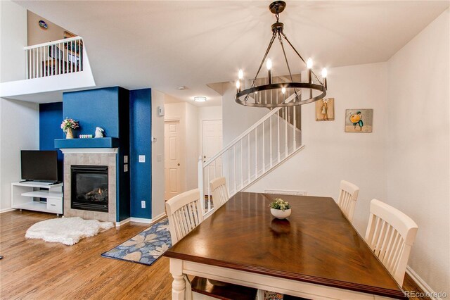 dining space featuring wood finished floors, a chandelier, stairs, baseboards, and a tiled fireplace