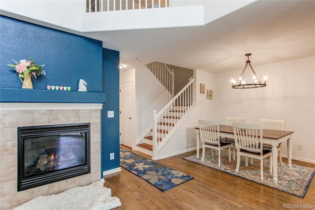 dining room featuring wood finished floors, a tiled fireplace, baseboards, a chandelier, and stairs
