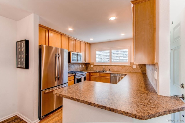 kitchen featuring stainless steel appliances, a peninsula, a sink, tasteful backsplash, and light wood-style floors