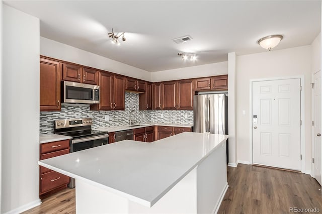 kitchen with stainless steel appliances, light countertops, decorative backsplash, and wood finished floors