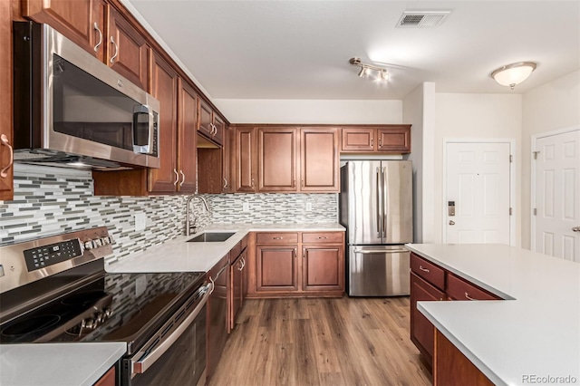 kitchen featuring appliances with stainless steel finishes, a sink, tasteful backsplash, and wood finished floors