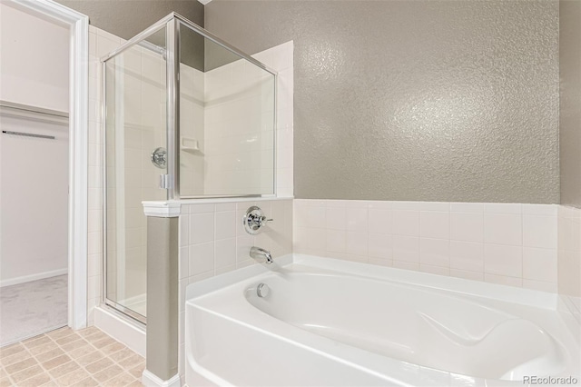 bathroom with a textured wall, a stall shower, and a garden tub