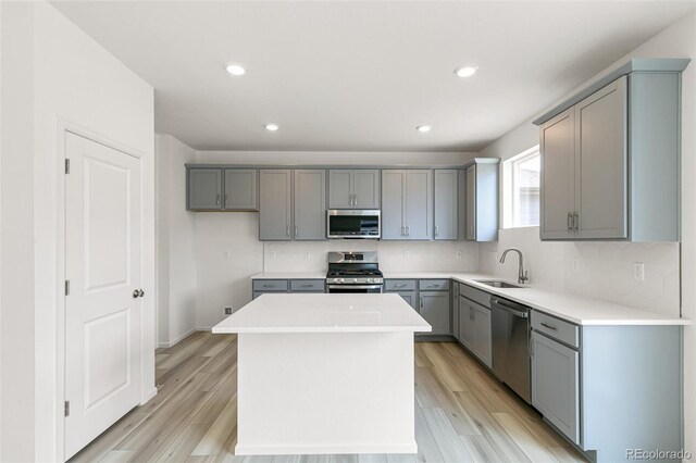 kitchen featuring gray cabinets, a sink, stainless steel appliances, backsplash, and a center island