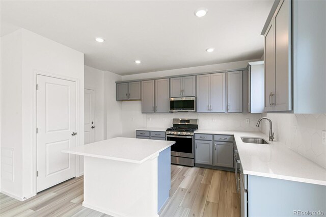 kitchen with gray cabinets, a sink, light wood-style floors, appliances with stainless steel finishes, and backsplash