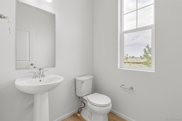 half bath featuring toilet, wood finished floors, baseboards, and a sink