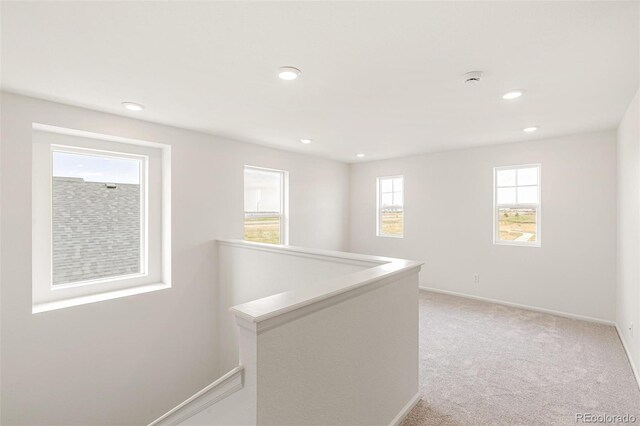 hall with an upstairs landing, recessed lighting, light colored carpet, and baseboards