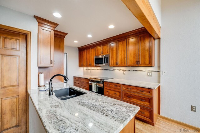 163 Ward Ct, Lakewood, CO 80228 - kitchen featuring stainless steel appliances, a sink, a peninsula, tasteful backsplash, and light stone counters