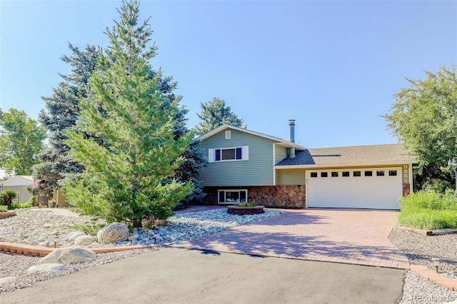 split level home with an attached garage, stone siding, and decorative driveway