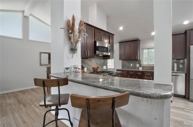 kitchen featuring kitchen peninsula, backsplash, stainless steel appliances, light hardwood / wood-style flooring, and a breakfast bar area