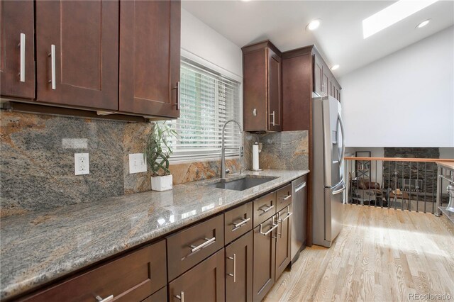 kitchen with light stone countertops, appliances with stainless steel finishes, light wood-type flooring, tasteful backsplash, and sink