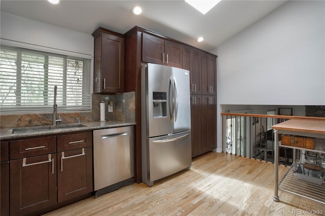 kitchen featuring dark brown cabinetry, sink, light hardwood / wood-style flooring, dark stone countertops, and appliances with stainless steel finishes