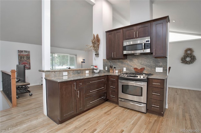 kitchen featuring kitchen peninsula, light stone counters, dark brown cabinets, stainless steel appliances, and light hardwood / wood-style flooring