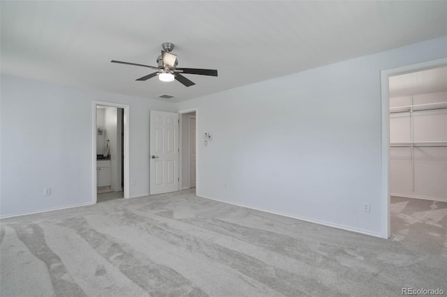 unfurnished bedroom featuring a spacious closet, a closet, ceiling fan, and light carpet