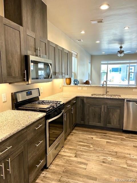 kitchen with light stone counters, ceiling fan, sink, light hardwood / wood-style flooring, and appliances with stainless steel finishes