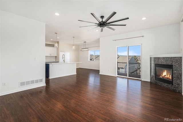 unfurnished living room with dark wood-type flooring, a ceiling fan, visible vents, and a tile fireplace