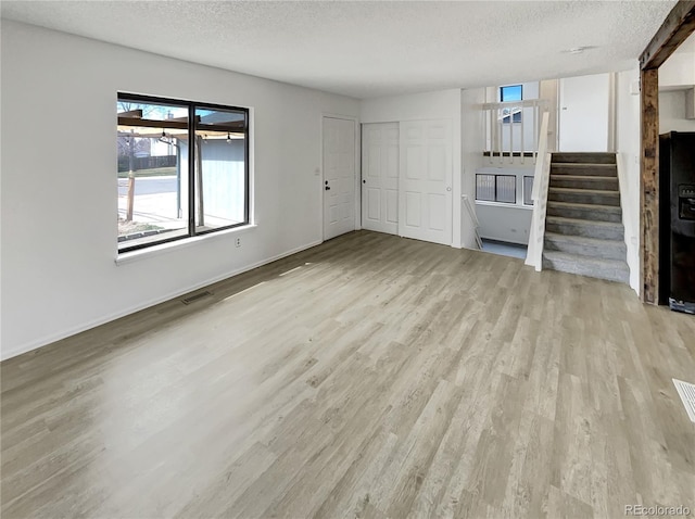 unfurnished living room featuring wood finished floors, baseboards, visible vents, stairs, and a textured ceiling