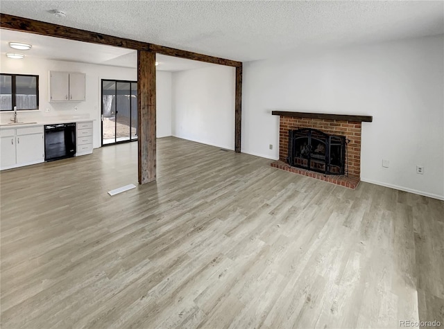 unfurnished living room featuring beamed ceiling, light wood-type flooring, a fireplace, a textured ceiling, and a sink