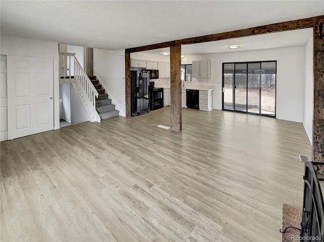 unfurnished living room featuring stairway, visible vents, light wood-type flooring, and a textured ceiling