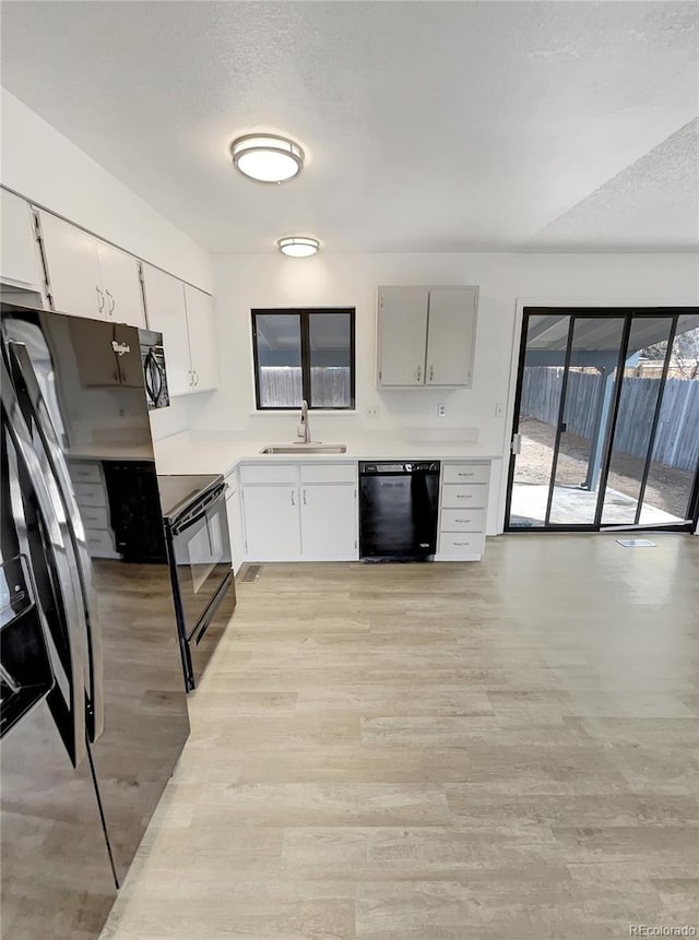 kitchen with black appliances, light countertops, light wood-style flooring, a textured ceiling, and a sink