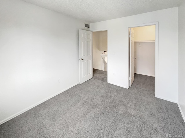 unfurnished bedroom with a walk in closet, baseboards, carpet floors, and a textured ceiling