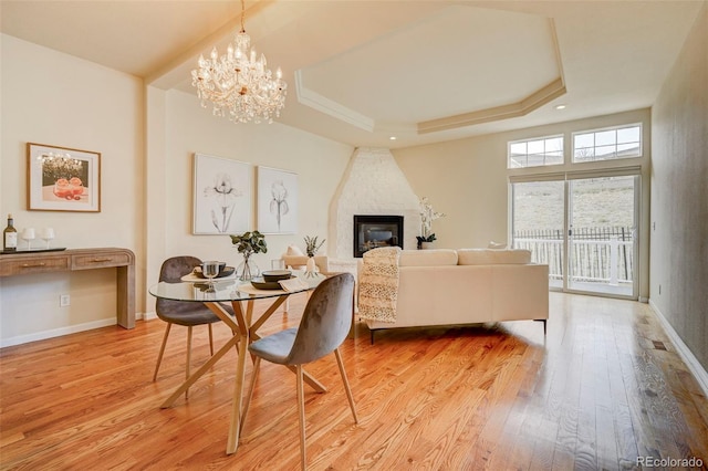 2061 Cheyenne Summer Vw, Colorado Springs, CO 80904 - dining space featuring a raised ceiling, light wood-style floors, a large fireplace, a chandelier, and baseboards