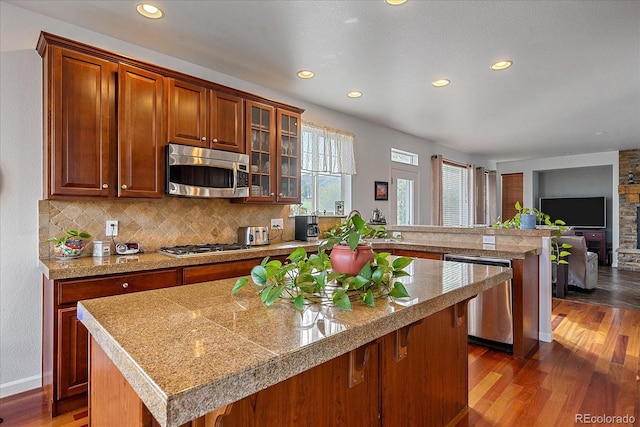 kitchen with a stone fireplace, backsplash, appliances with stainless steel finishes, dark hardwood / wood-style floors, and a center island