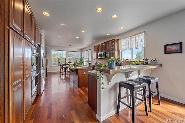 kitchen with kitchen peninsula, appliances with stainless steel finishes, a kitchen bar, and dark hardwood / wood-style flooring