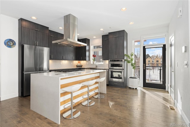 kitchen featuring island exhaust hood, a kitchen island, a breakfast bar, stainless steel appliances, and dark hardwood / wood-style floors