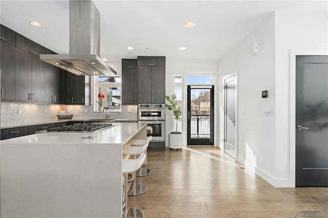 kitchen with a kitchen bar, island range hood, a kitchen island, light hardwood / wood-style flooring, and stainless steel appliances