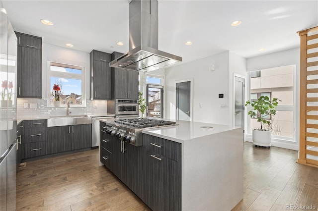 kitchen with appliances with stainless steel finishes, sink, island exhaust hood, a center island, and decorative backsplash