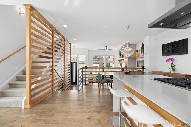 kitchen with ceiling fan, decorative light fixtures, wall chimney exhaust hood, light hardwood / wood-style floors, and stainless steel gas cooktop