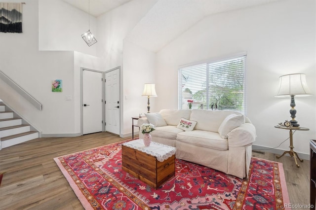 living area featuring wood finished floors, stairs, high vaulted ceiling, and baseboards