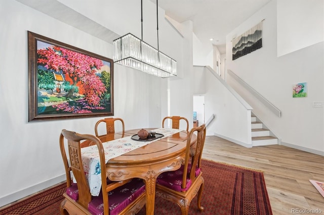 dining area with wood finished floors, a chandelier, stairs, baseboards, and a towering ceiling