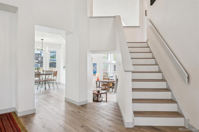 stairs featuring healthy amount of natural light, wood finished floors, a chandelier, a towering ceiling, and baseboards